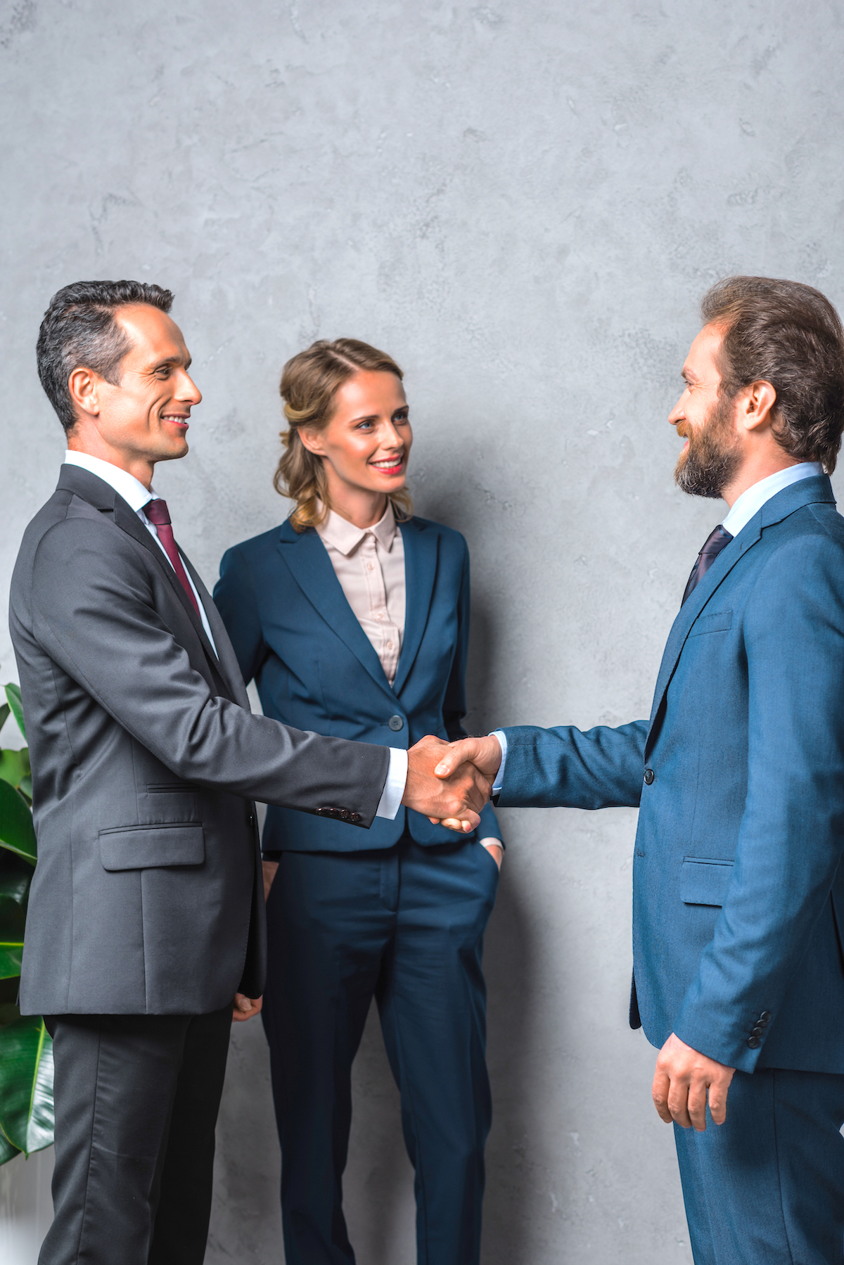 side view of smiling business people shaking hands with colleague standing near by